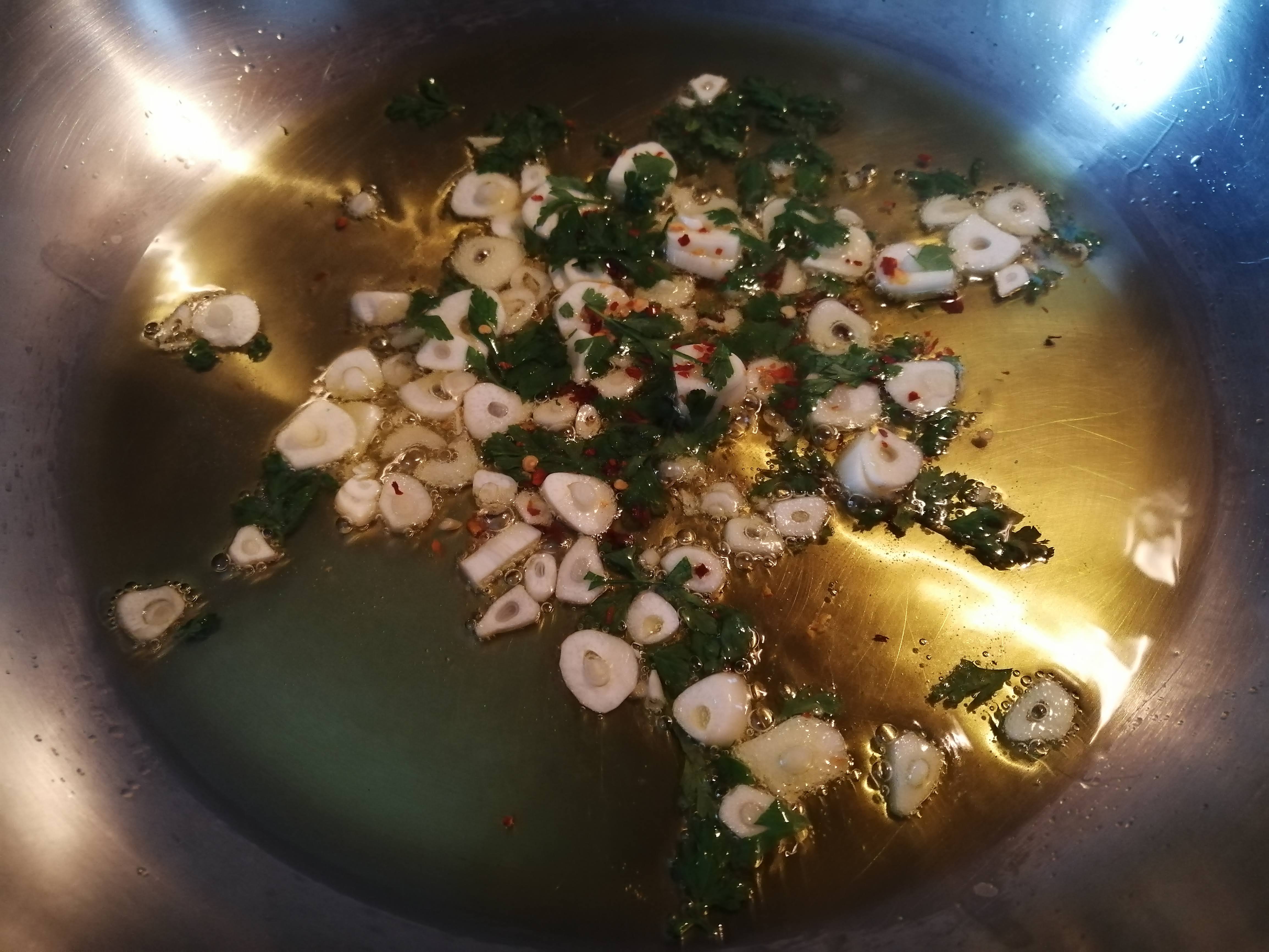 Na panvicu nalejeme olivový olej a pridáme nakrájané strúčiky cesnaku a trochu nasekanej petržlenovej vňate.