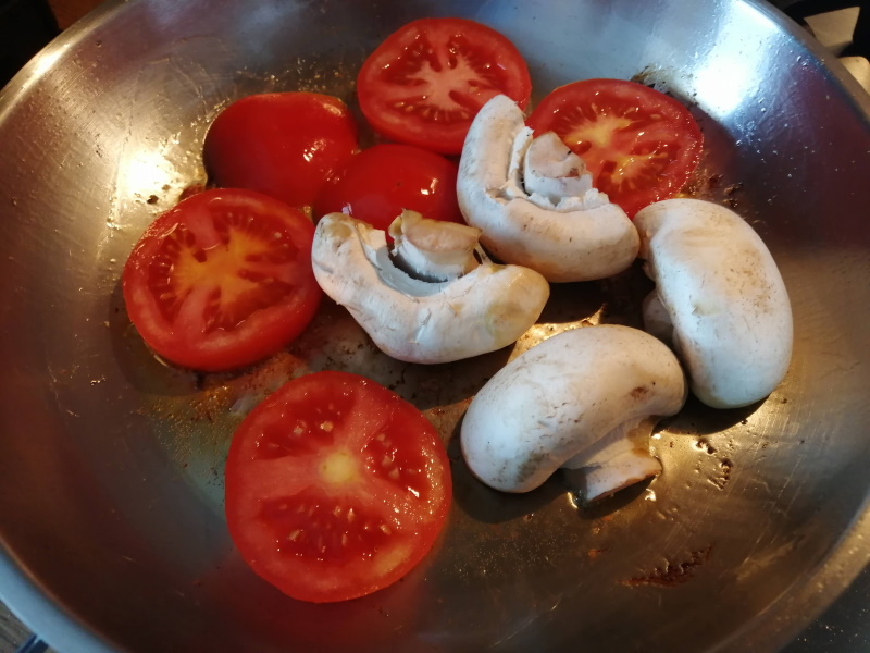 Pridáme do panvice nakrájané paradajky na plátky a šampiňóny na polovice.