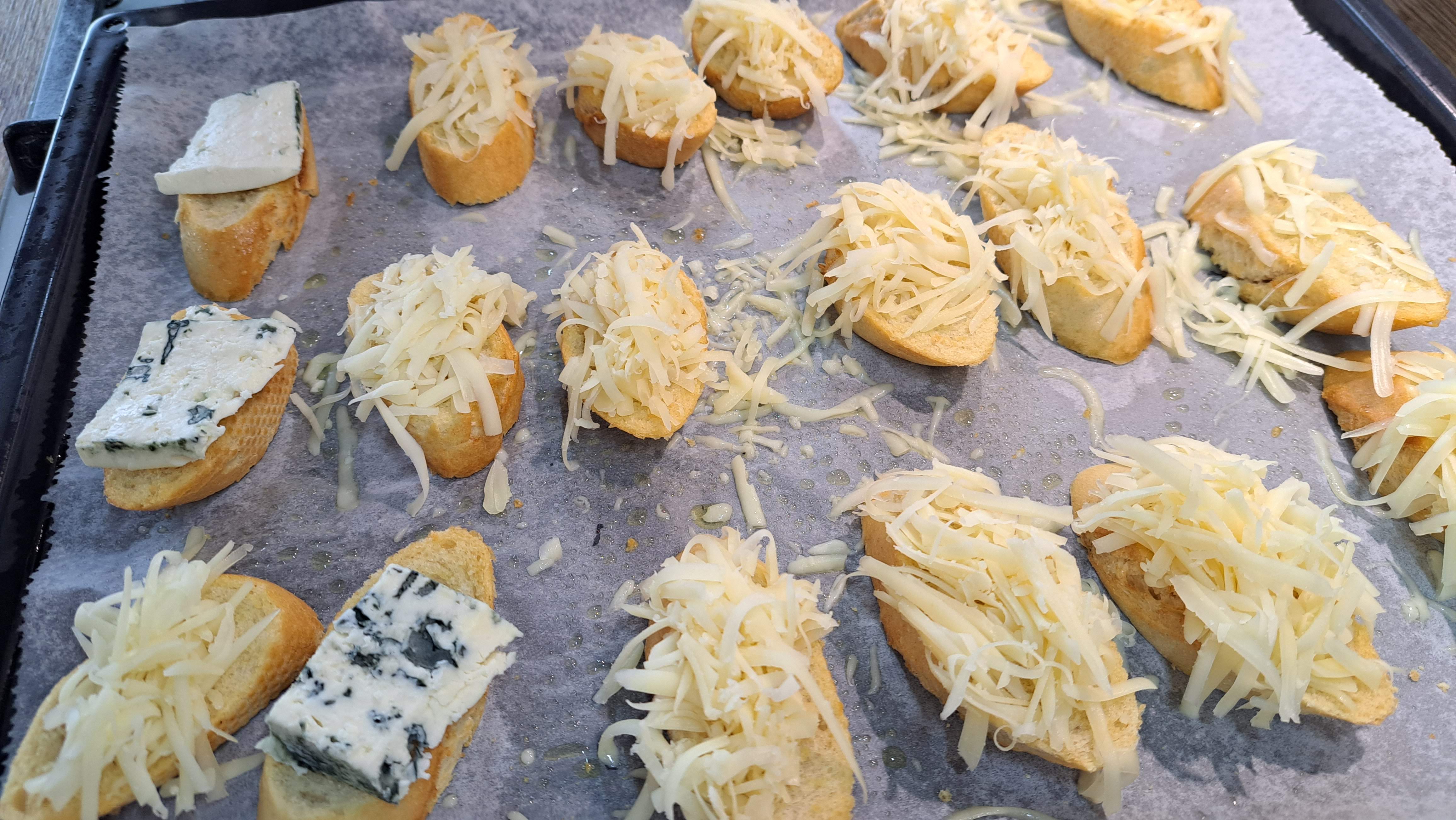 Na opečené bagety naložíme nastrúhaný tvrdý syr, prípadne aj nakrájanú nivu a vrátime do rúry s horným grilom na zapečenie